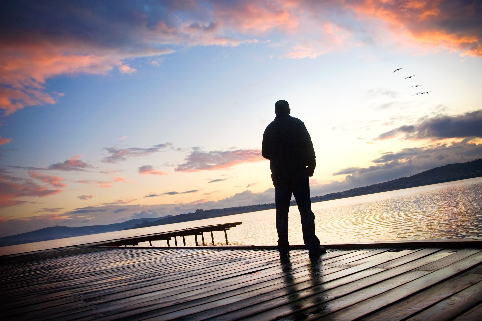 Rear view single man on wooden dock looking at seascape view during sunrise